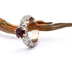 Ring with floral patterned band and red garnet gemstone in prong setting