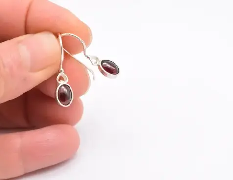Small oval garnet silver earrings with tiny heart on top. Μικρά κρεμαστά σκουλαρίκια με γρανάδα και μικρή καρδούλα στην κορυφή