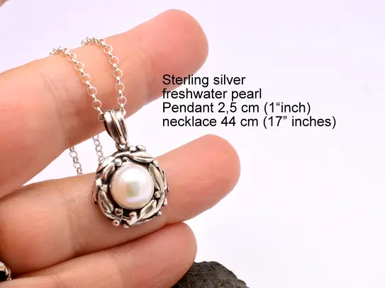 Close-up of a handmade sterling silver freshwater pearl pendant necklace on a 17-inch chain. The round pearl is set in a detailed leaf or wreath design.