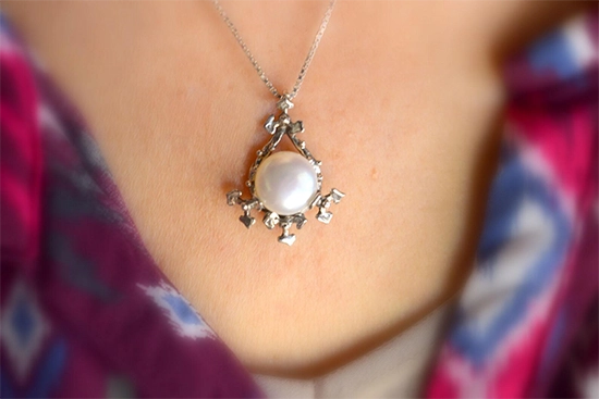 Floral pearl pendant necklace worn at collarbone on woman's neck